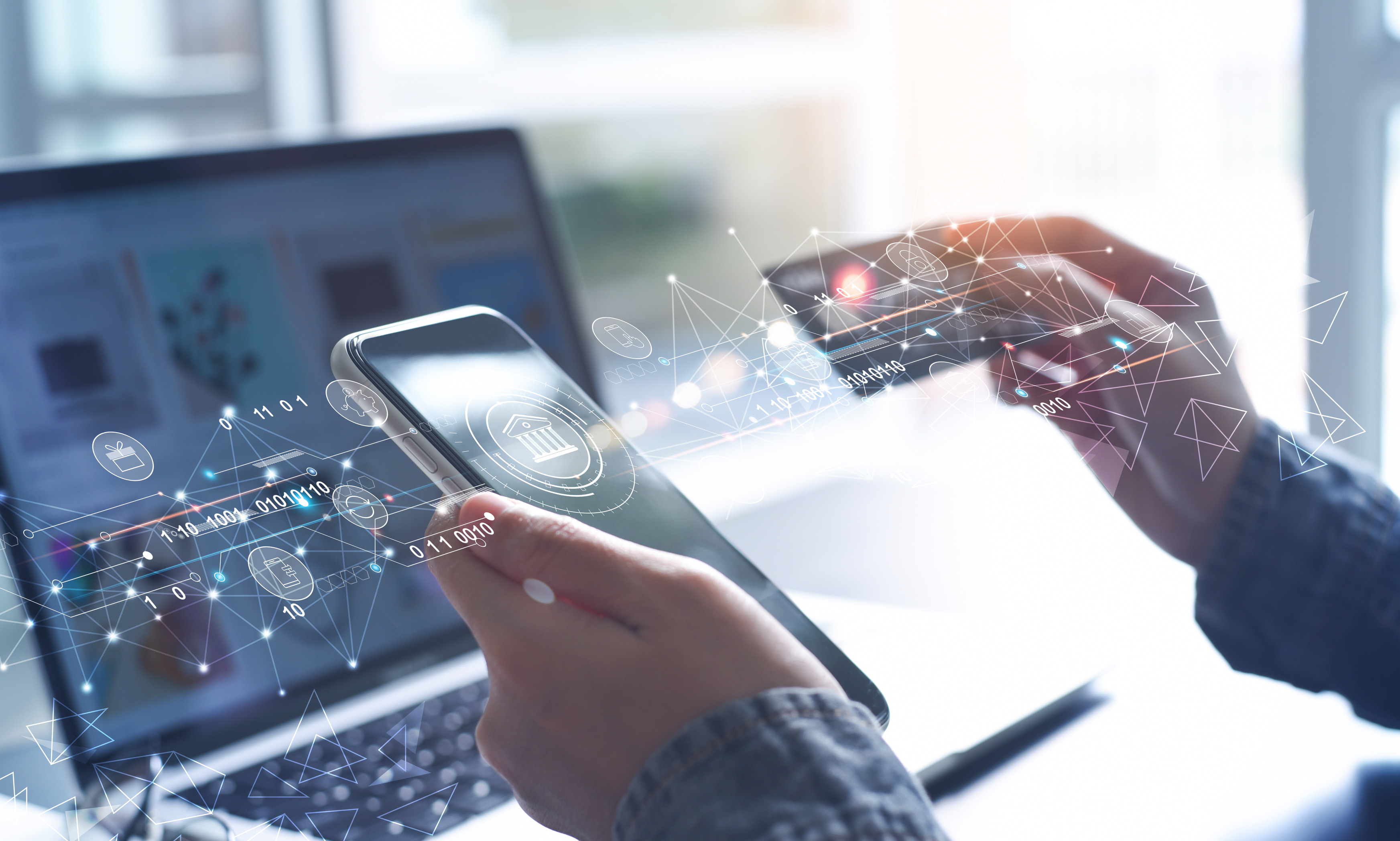 A set of hands holding a smart phone over a computer, holding a credit card over the smartphone and light streams connecting the two