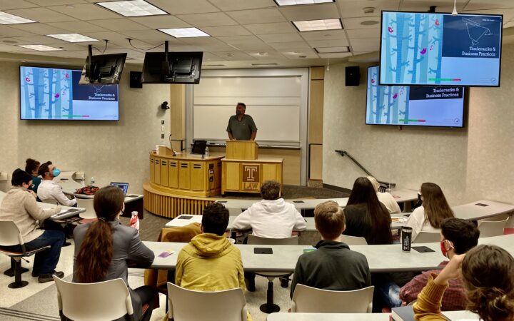 Man stands at podium speaking to a classroom full of students