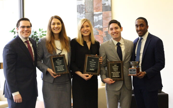 five smiling people dressed in business attire and holding three plaques and a trophy
