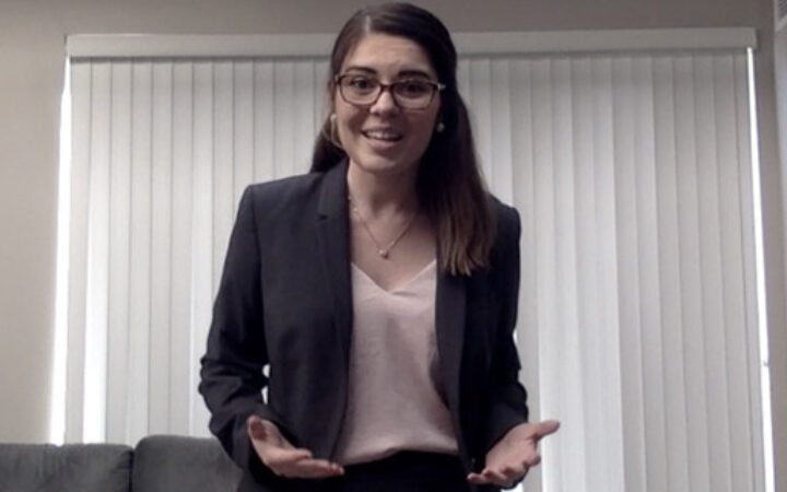 Young woman with long hair wearing glasses and business attire, speaking with open hands