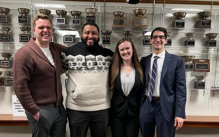 Four Temple Law Students stand smiling in front of a trophy case
